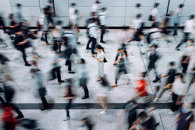 A person looking at their phone while a blurred crowd rushes past